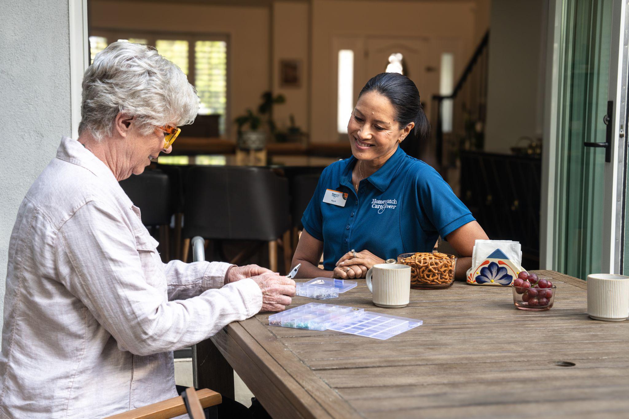 A female caregiver sits at outside table with elderly woman to help with her medication managment.