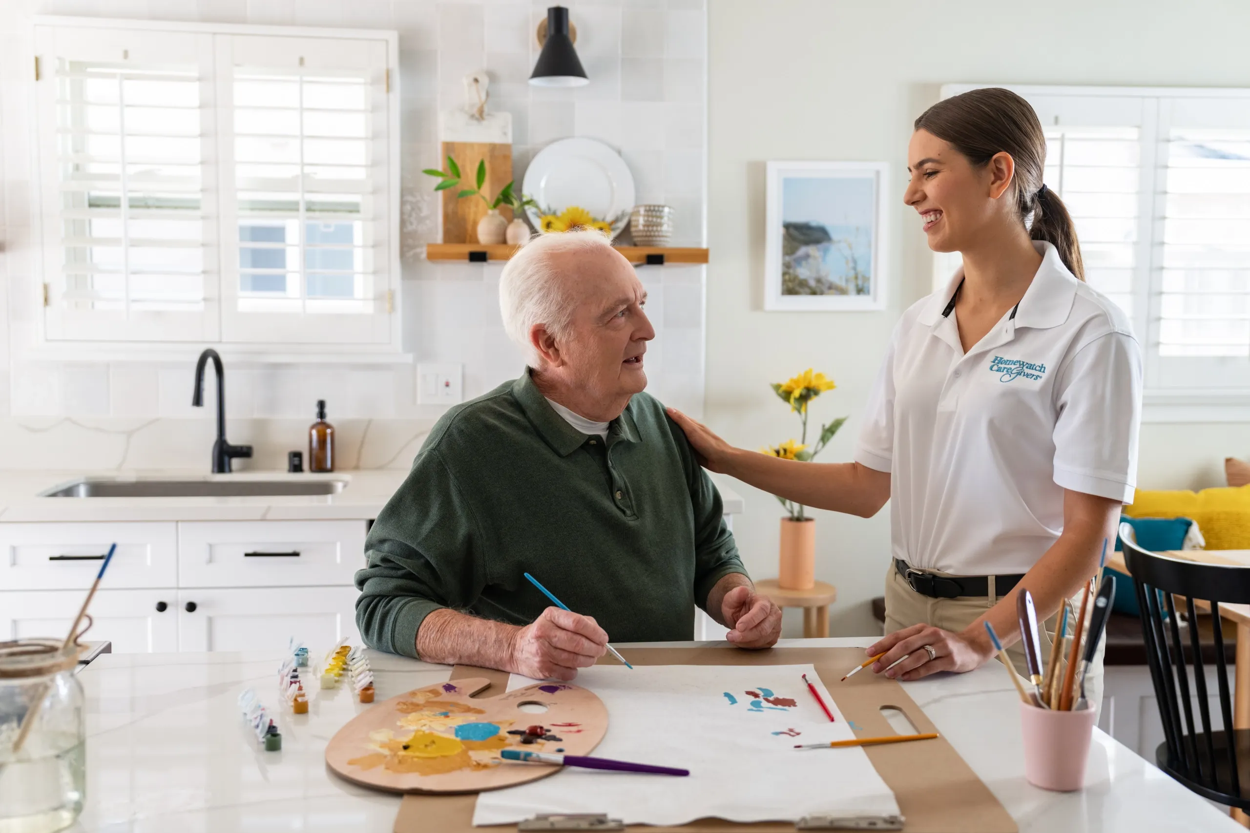 An elderly man sitting in the kitchen with a caregiver