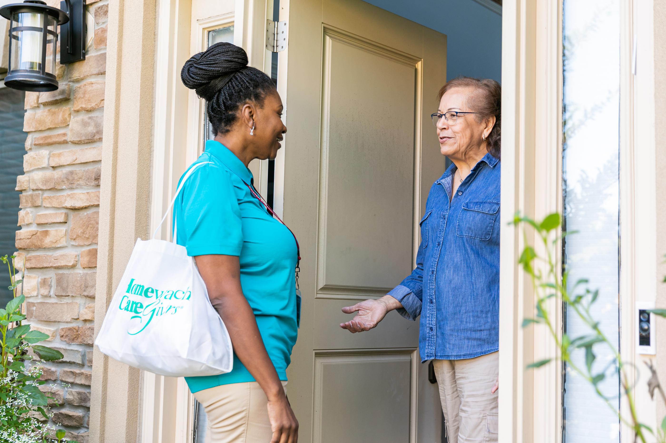 Caregiver standing outside home talking to older woman