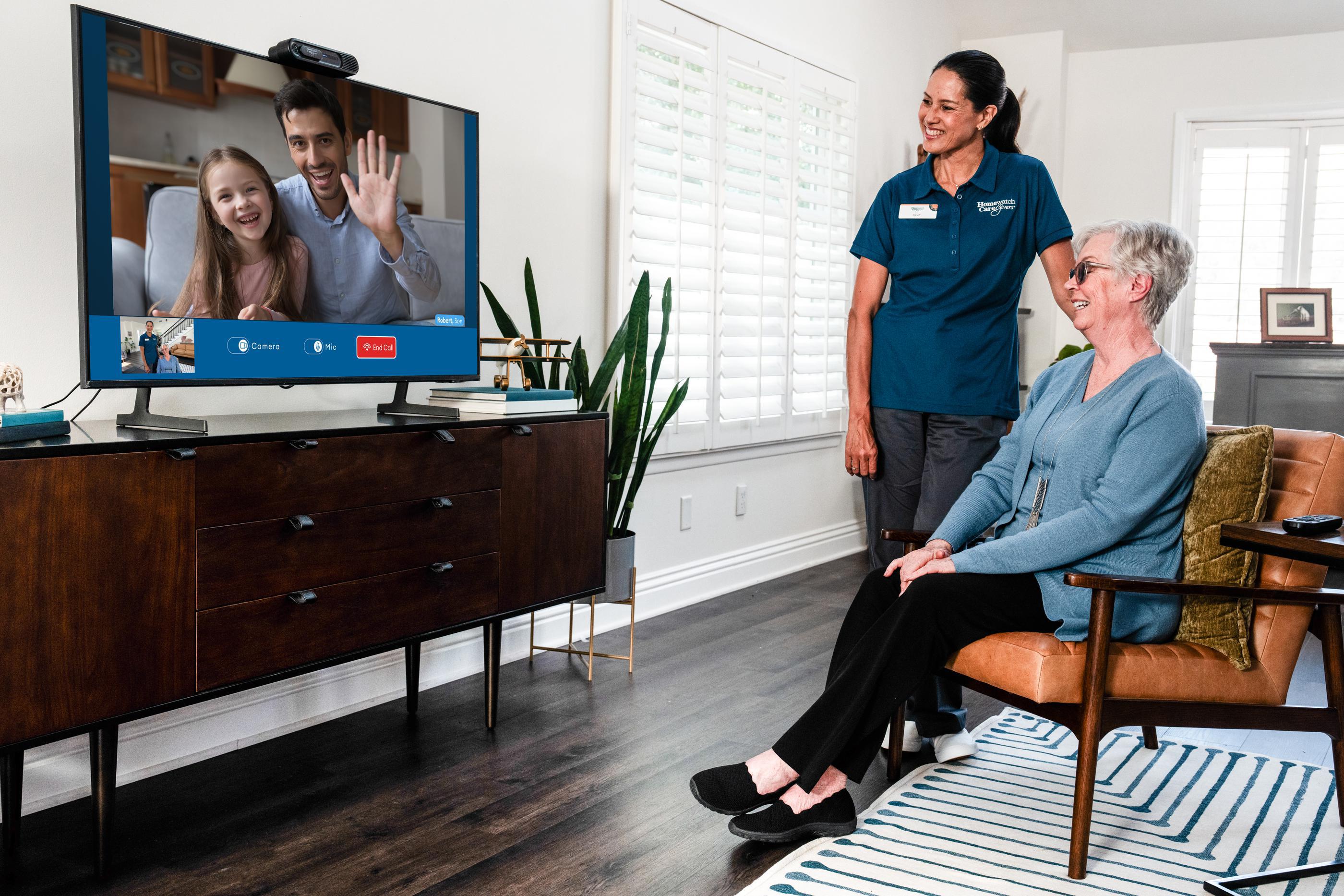 caregiver standing next to woman in chair, both looking at virtual call screen