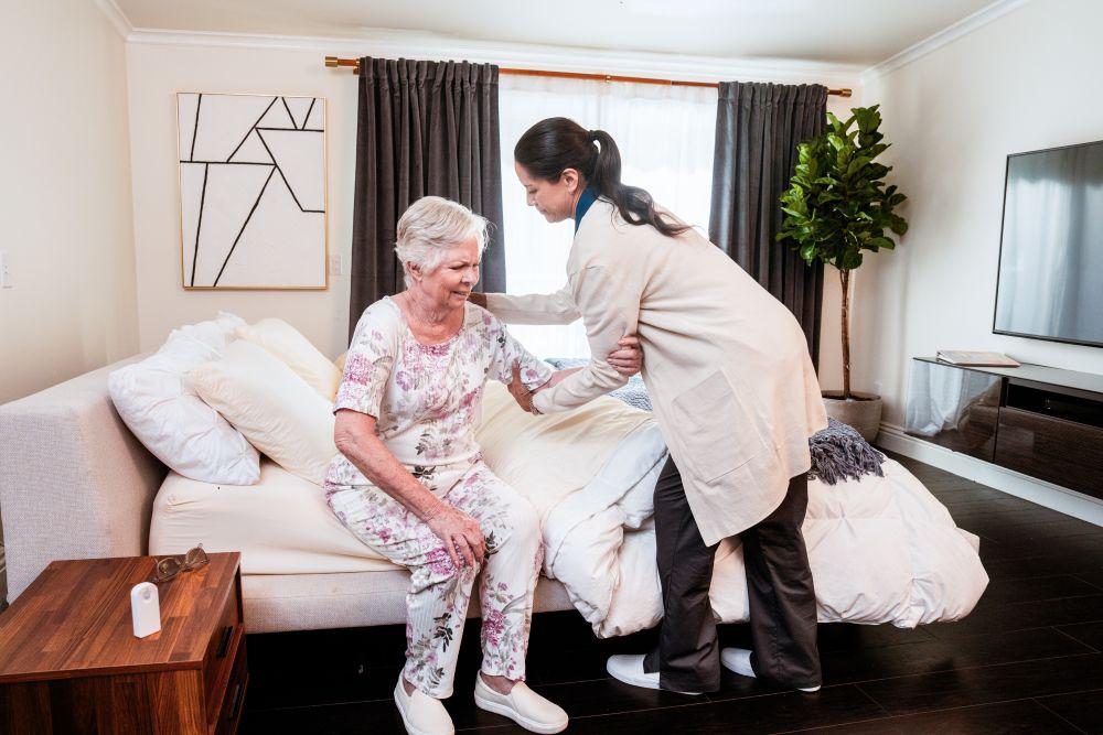 female caregiver helping older woman get out of bed