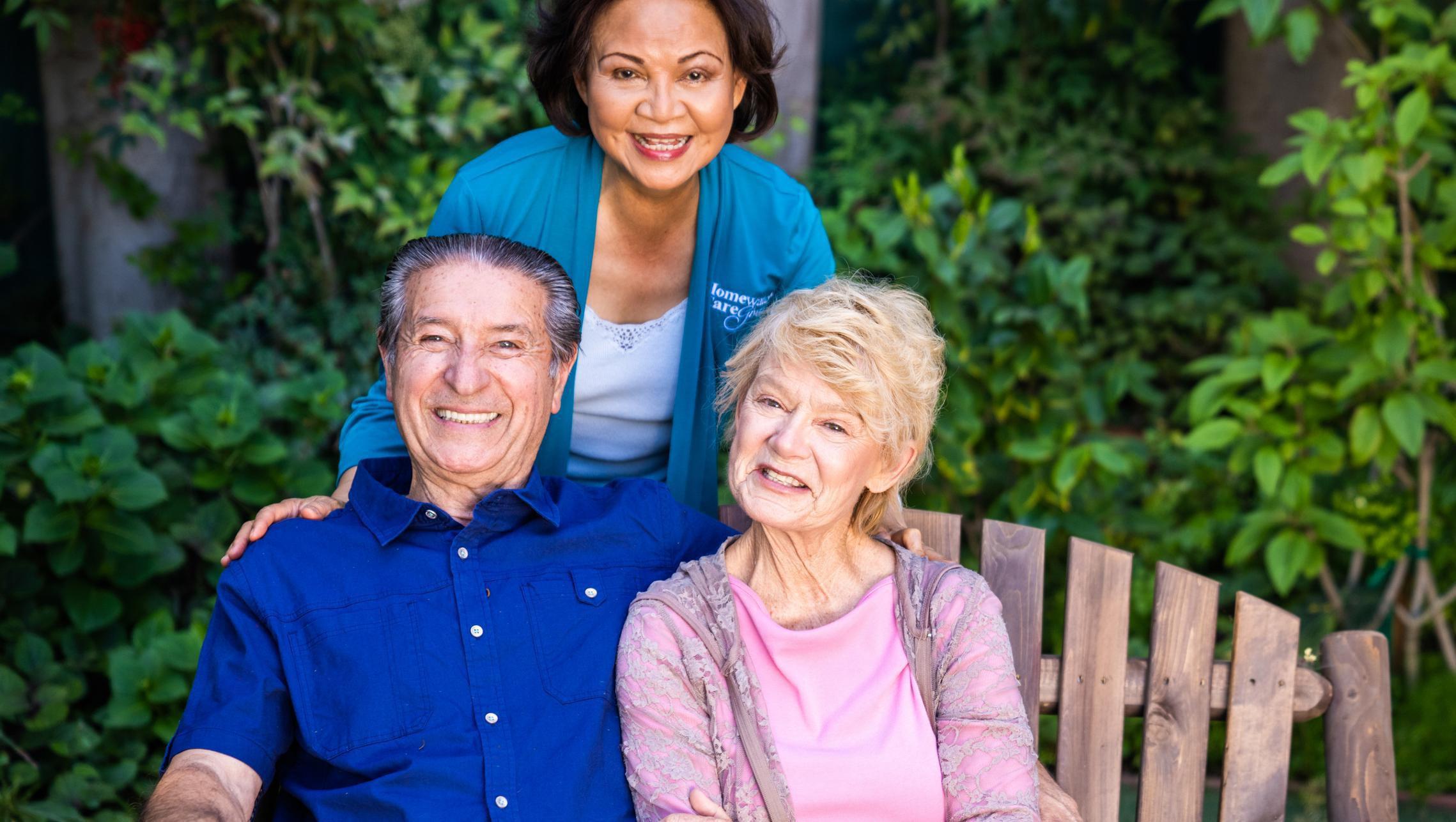 couple sitting on bench with caregiver behind them