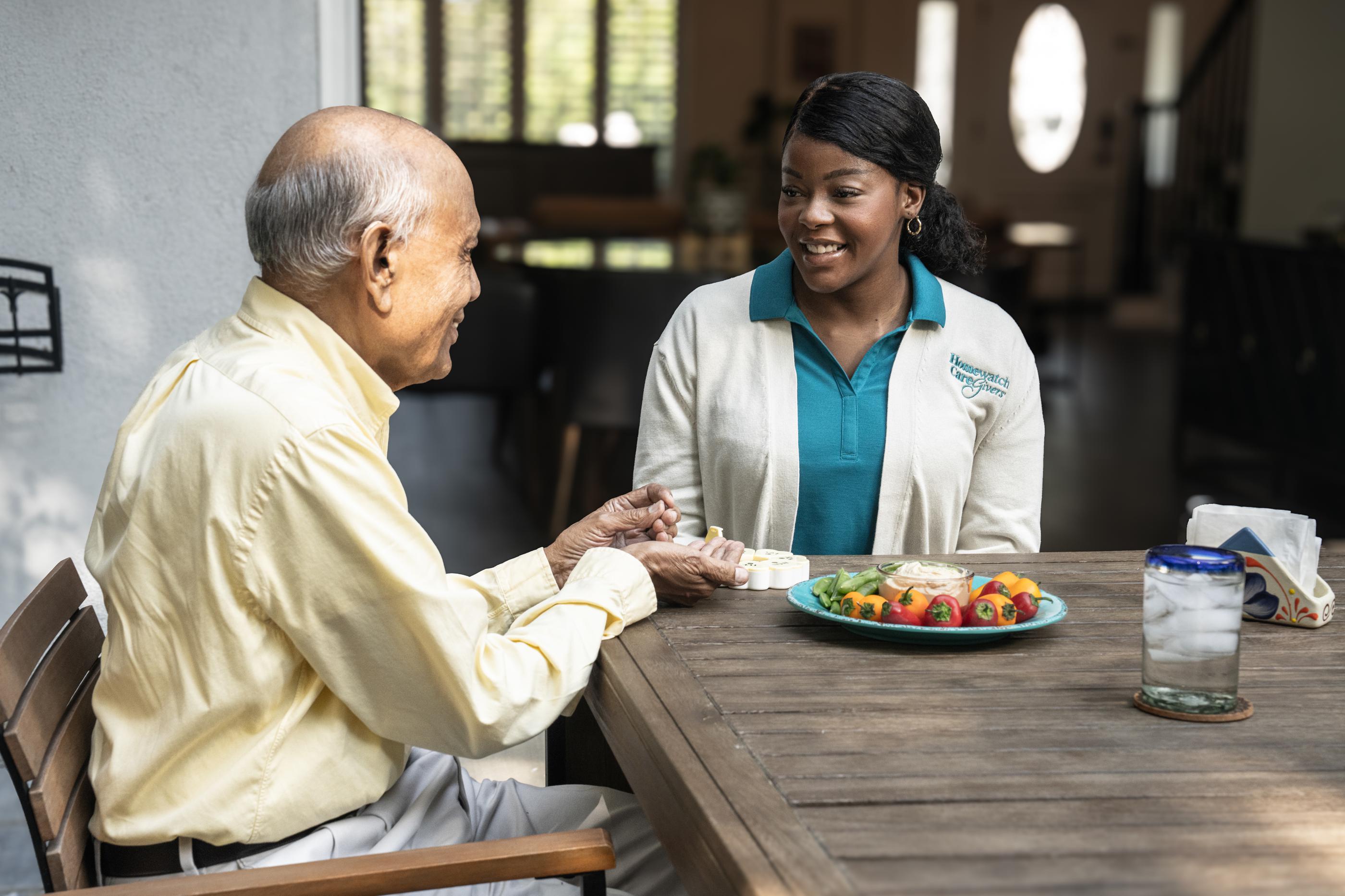 female caregiver helping older man sort his medications at oudoor dining table