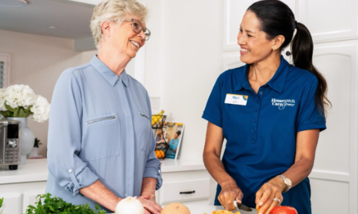 woman and caregiver smiling at eachother chopping vegetables