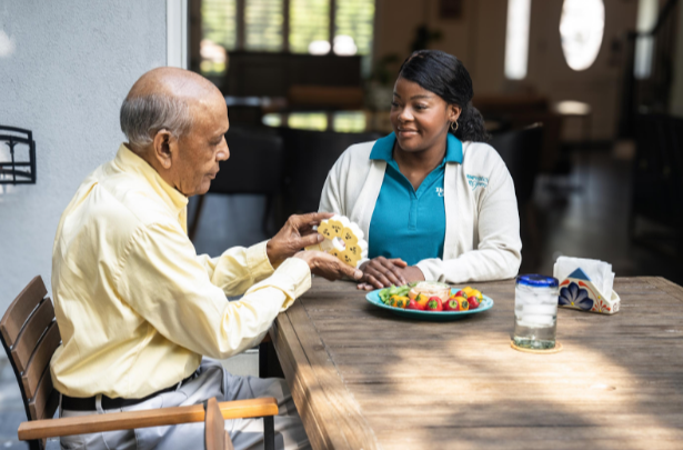 man taking pills out of container with caregiver smiling next to him